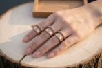 Bronze tone ring set of valknut stamped bands and twisted open cuffs worn on a hand resting on a sawn log with an oak tray