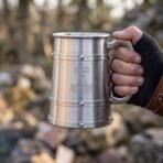 Brushed stainless steel tankard with an etched Mjolnir and riveted bands held by the handle in a fingerless gloved hand