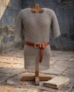Butted mild steel chainmail hauberk with short sleeves and a thigh length skirt, hung on a wooden stand with a leather belt and a folded gambeson.