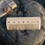 Carved bone comb with Celtic knotwork, ring and dot roundels and copper rivets lying flat on a dark stone by a linen pouch
