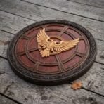 Carved hardwood round shield with pale double headed eagle on a red brown spoked face lying on old wooden boards