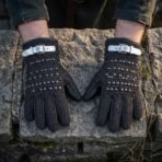 Chainmail and black leather gauntlets with domed steel studs and buckled cuffs resting palms down on a rough stone wall