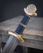 Close up of a brass Viking sword hilt with Vegvisir disc pommel, blue leather grip and twisted brass wire rings