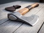 Close up of a Damascus bearded axe head with engraved lozenge panel and polished steel poll on weathered boards