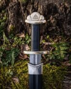Close up of a Damascus steel Viking sword hilt with triquetra engraved brass pommel and brass guard above a black scabbard
