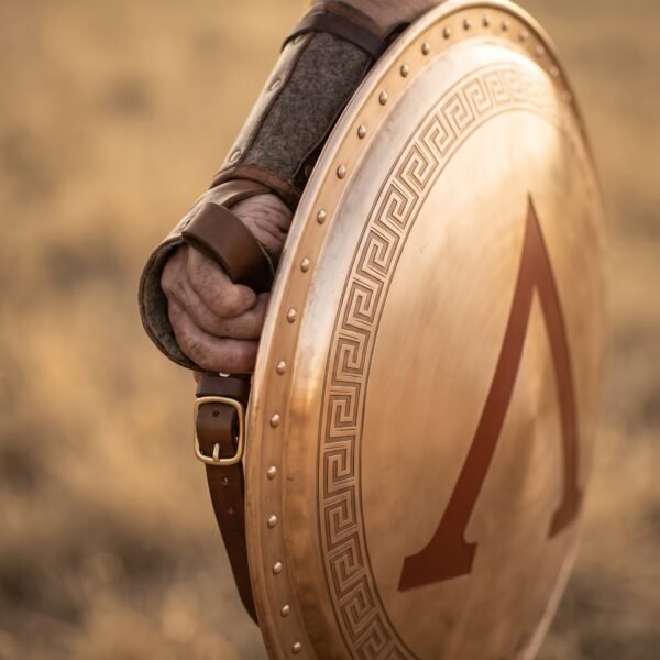 Close up of a Spartan shield with red lambda and meander border held on the forearm by leather straps in warm evening light