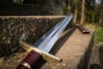Close up of a steel sword with brass crossguard, oxblood leather grip and etched knotwork panel lying on stone steps