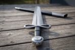 Close up of the polished infinity loop guard, black grip and Mjolnir engraved pommel of a Damascus sword