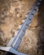 Close up of a wavy Damascus flamberge blade showing the flowing pattern below a flat steel crossguard