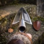 Close view down the socket of a polished steel spearhead with knotwork panel and runes, leather cover behind