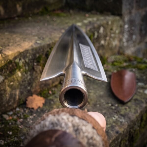 Close view down the socket of a polished steel spearhead with knotwork panel and runes, leather cover behind