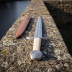 Close view of a cord wrapped arming sword from the pommel end, the engraved circular knot on the steel disc and the cream cord winding on the grip
