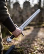 Close view of a Damascus arming sword with Helm of Awe engraved below a flat guard and a wheel pommel in a hand