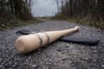 Close view of the barbed wire bands wrapped around the barrel of an ash bat on gravel with the canvas sleeve behind