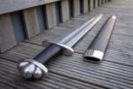 Close view of the hilt of a celtic knot panel viking sword, the three lobed polished pommel, black leather grip and the steel throat of the black scabbard