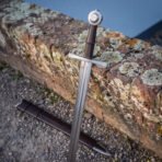 Close view of the hilt of a wheel pommel knightly sword, the steel disc pommel and risered brown leather grip set against orange lichen on an old sandstone wall