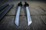 Close view of the twin ninjato set from the blade tips, showing the straight angled kissaki, bright polished flats, round tsuba and black cord wrapped handles above.