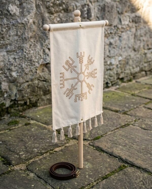 Cream cotton canvas banner with a vegvisir print, turned ash cross bar and tassel fringe hung on a wooden pole against a stone wall