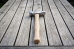 Cross pein forging hammer with polished steel head and pale hickory handle laid flat on a slatted table