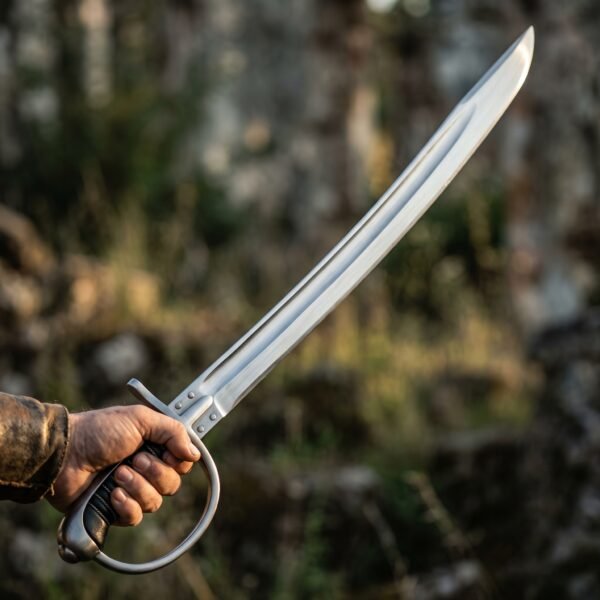 Curved sabre trainer with stirrup hilt and black grip held out in hand against a blurred woodland backdrop