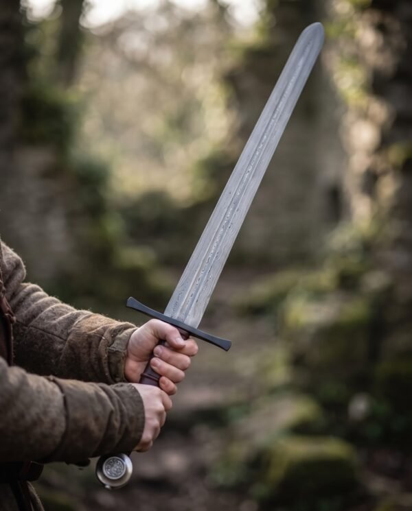 Damascus arming sword with rounded point, dark spatulate guard and burgundy grip held upright in a forest
