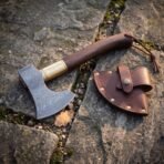 Damascus bearded axe with runed brass collar and wood haft lying on flagstones next to its riveted leather sheath