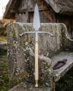 Damascus boar spear standing upright against a lichen covered stone bench with its leather blade cover