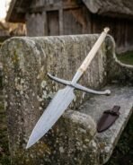 Damascus boar spear with ball tipped crossbar and ash haft leaning on a mossy stone bench beside a leather cover
