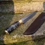 Damascus broken back seax with horn grip and brass pommel, close angled view of the handle and blade beside a brown leather sheath