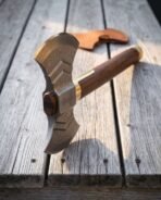 Damascus double headed axe with engraved Mjolnir cheek, walnut haft and brass collar on grey boards by a leather cover