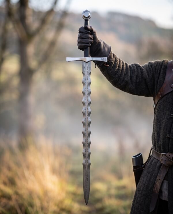 Damascus flame bladed sword held upright by the grip in a gloved hand with a misty valley behind