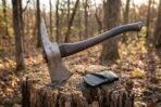 Damascus hatchet with rune line on the head embedded in a tree stump in autumn woods, black leather mask beside