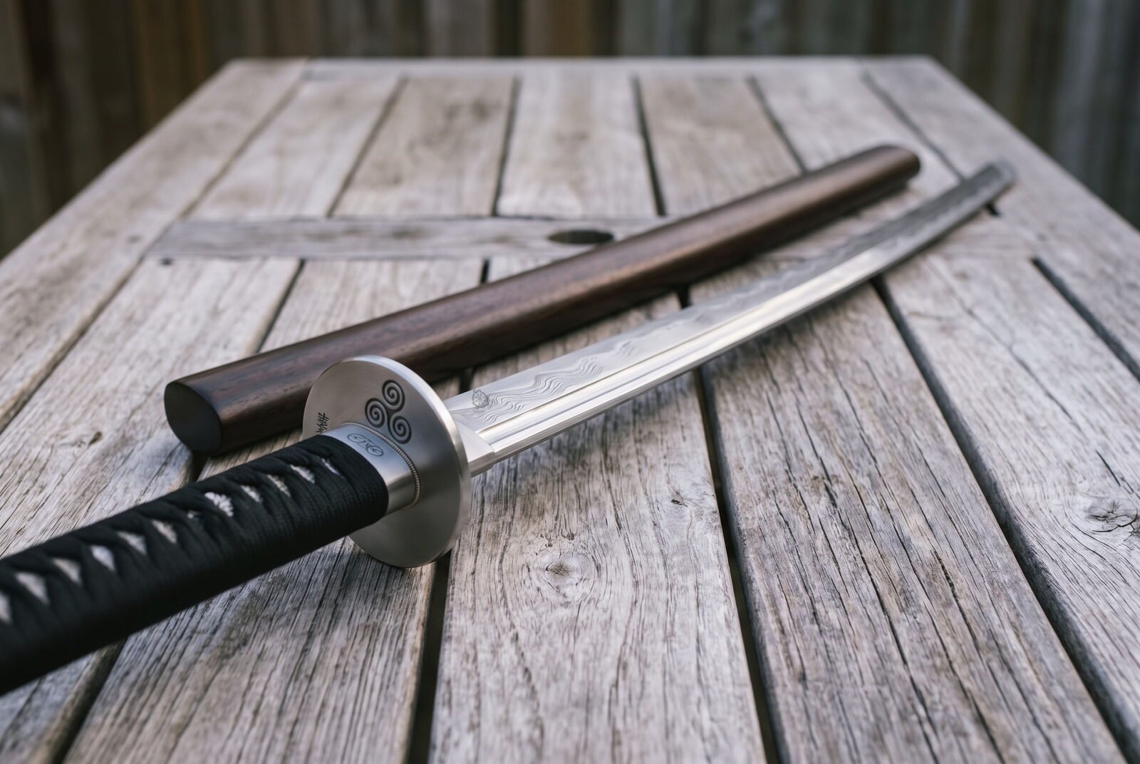 Damascus katana sword lying on weathered decking beside its dark hardwood saya, the triple spiral guard and grooved laye Damascus katana sword lying on weathered decking beside its dark hardwood saya, the triple spiral guard and grooved layered blade catching low afternoon light