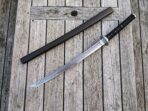 Damascus katana with black cord wrapped handle and round steel tsuba laid beside its dark wooden saya on planks