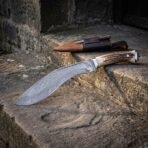 Damascus kukri with stag antler grip, wider view across old stone steps with the sheath holding karda and chakmak on the step above