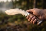 Damascus kukri with rosewood scales, steel bolster etched with a wolf and steel butt cap held in a hand in misty woods