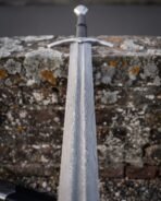 Damascus longsword close up of the pattern welded blade and curved crossguard against a mossy brick wall