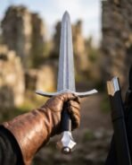Damascus longsword held point up in a leather gloved hand showing the faceted pommel and curved guard