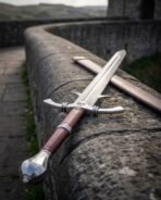 Damascus longsword with barbed quillons and a fluted pommel laid along the top of a curved stone wall over a valley