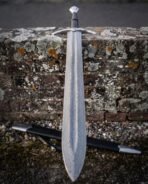 Damascus longsword with crown pommel and curved crossguard leaning point down on a lichen covered brick wall