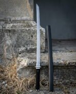 Damascus ninjato with a straight pattern welded blade, spiral engraved round guard and black cord handle standing beside its lacquered scabbard on stone steps