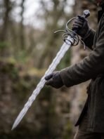 Damascus steel flame bladed sword with blackened swept hilt held across the body in gloved hands among ruins
