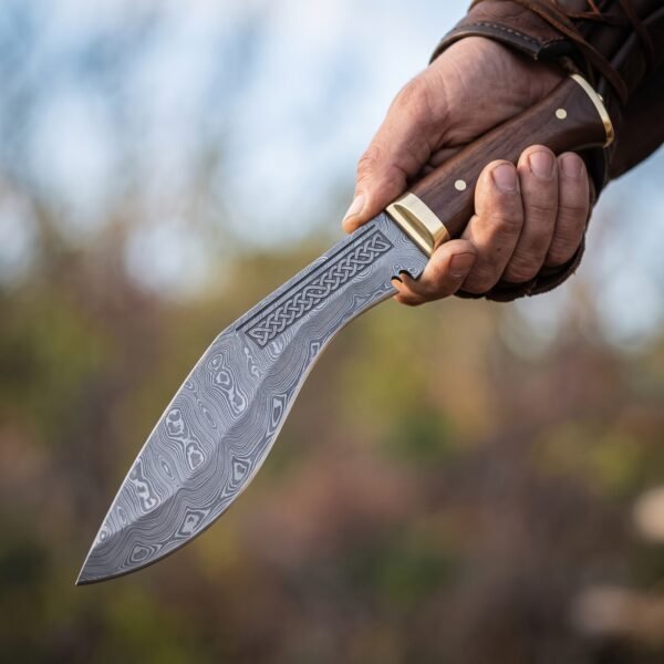 Damascus steel kukri knife with etched knotwork panel, brass bolster and dark wood handle held up in one hand outdoors