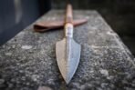 Damascus steel spear head with leaf shaped blade and engraved steel socket on an ash haft resting on a stone ledge