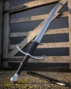 Damascus steel two handed longsword with parrying hooks and ring tipped crossguard leaning on a wooden farm gate