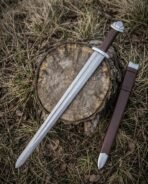 Damascus steel Viking short sword with lobed steel pommel and brown leather grip lying on a stump beside its brown scabbard