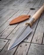 Damascus steel Viking spear head with riveted socket, close up on weathered boards beside a tan leather blade cover