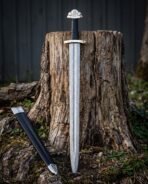 Damascus steel Viking sword standing against an old tree stump next to its black scabbard with steel fittings