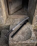 Damascus steel wakizashi with round tsuba and black wrapped handle lying across a stone step next to its saya