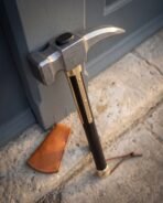 Damascus steel war hammer head and brass langets in close view, leaning on a door frame with a tan leather cover